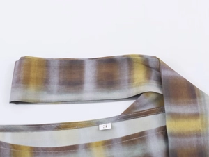 Détail du motif à carreaux et de l'étiquette taille S sur le poncho en maille pour femme