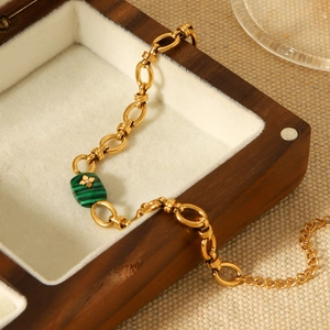 Macro detail of gold chain bracelet with green malachite pendant on wooden box