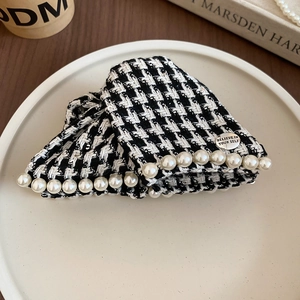 Detail of houndstooth fabric hair claw with white pearls and engraved metal charm