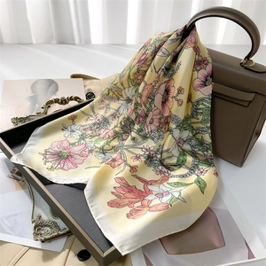 Elegant floral silk scarf with pink flowers on yellow base displayed with a handbag