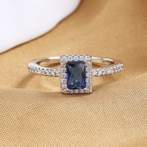 Macro shot of rectangular blue zircon ring with halo crystals on satin background