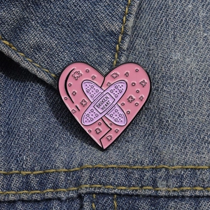 Close-up of pink heart enamel pin with Broken Heart text pinned on blue denim pocket