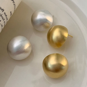 Matte gold and silver dome stud earrings with brushed metallic texture on a ceramic plate