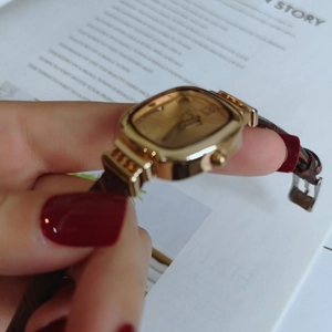 Detailed close-up of a square gold watch dial with a textured deep red leather strap