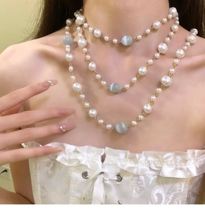 Detail of baroque pearl and cat eye stone layered necklace worn on a woman neck