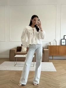 Close-up of a white cotton tie-neck blouse styled with high-waist blue denim jeans