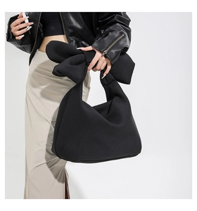 Detail of a large black bucket bag featuring an oversized decorative bow on the handle