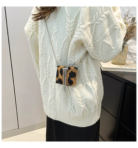 Close-up of leopard print mini crossbody bag with silver chain strap on white sweater