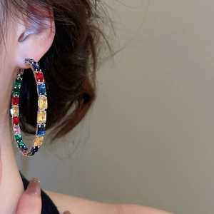 Close-up of model wearing large silver hoop earrings with vibrant rainbow rectangular zircons