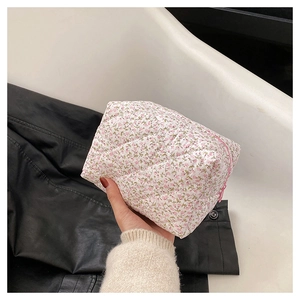 Detail of white quilted floral makeup bag with pink flowers held by a hand