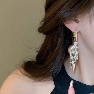 Close-up of sparkling tassel rhinestone drop earrings worn by a model in soft lighting