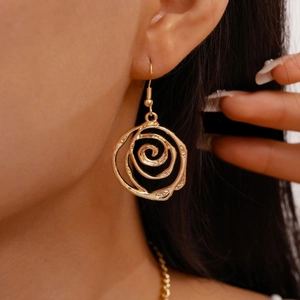 Close-up of golden hollow rose pendant earring worn by model with warm lighting