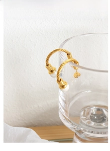 Detailed close-up of golden twisted rope texture earrings featuring elegant white pearls