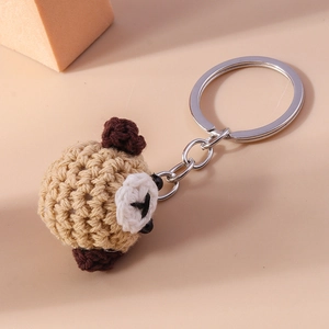 Close-up of a handmade knitted beige pug dog keychain with silver metal ring connector