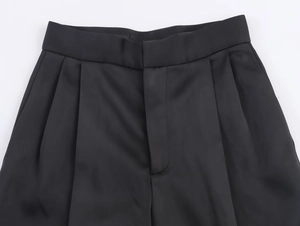 Dettaglio dei pantaloni in raso nero a vita alta con eleganti pieghe sul davanti