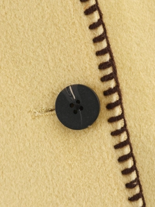 Detail of yellow wool fabric with black button and brown decorative stitching on the coat