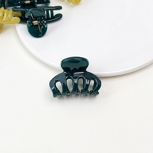 Close-up of translucent dark green jelly hair claw clip on a white ceramic plate