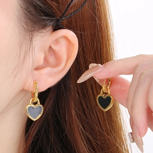Détails de boucles d'oreilles cœur dorées avec émail noir portées sur l'oreille