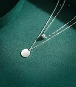 Macro shot of 925 sterling silver double-layered necklace with round pendant on green surface