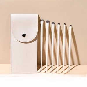 Detail of 6 mini makeup brushes with matte white handles and a cream leather pouch