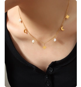 Detailed view of gold necklace with star and moon charms and freshwater pearls on model