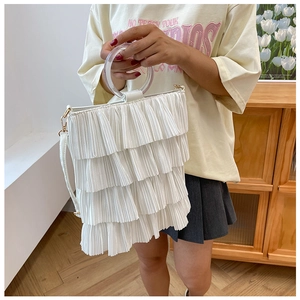 Detail of white tiered ruffle handbag featuring transparent acrylic handle and gold hardware