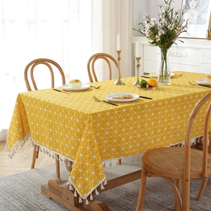 Detailed close-up of yellow cotton linen tablecloth with white triangles and beige tassels