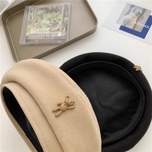 Close-up of wool beret with cute teddy bear ornament in beige and black colors