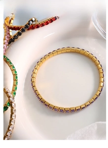 Close-up of gold-plated tennis bracelets with colorful square zircons on ceramic
