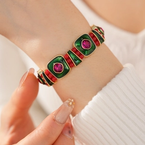 Close-up of vintage gold bangle with green enamel and red beads on a model's wrist