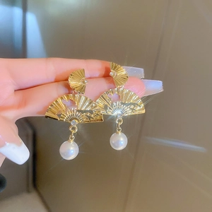 Gros plan de boucles d'oreilles éventail dorées avec strass et perles blanches
