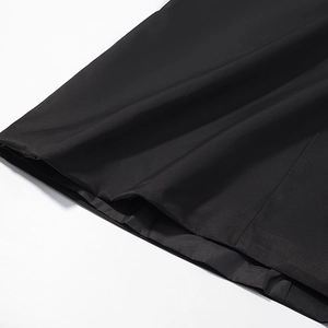 Detailed close-up of the smooth black fabric texture and hem stitching on the long coat