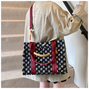 Detail of checkered tweed tote bag with fringe edges and vibrant red woven handles
