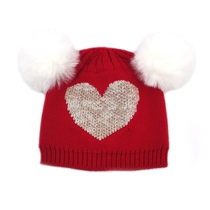 Detailed knit texture and dual white faux fur pom-poms on a red heart winter hat