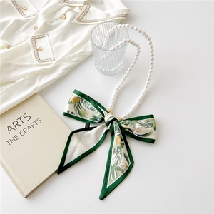 Detail of pearl necklace with green plant print silk scarf tied in a bow on white surface