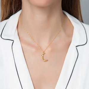 Detail of gold crescent moon pendant necklace worn on neck with white shirt background