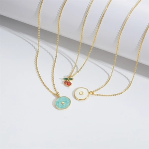 Minimalist gold necklaces with crab, star, and cherry pendants on a white display