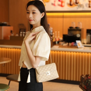 Sac à bandoulière beige matelassé avec chaîne dorée porté par un mannequin élégant