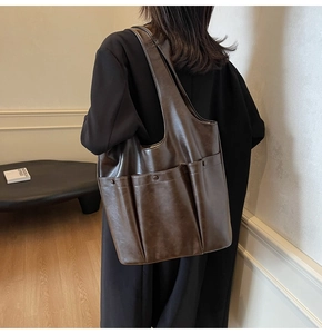 Close-up of a dark brown PU leather tote bag with large front pockets shown on model