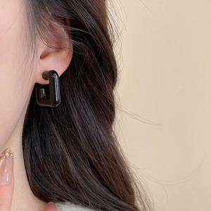 Macro side view of sleek black C-shaped acrylic earrings with a mirror-like finish