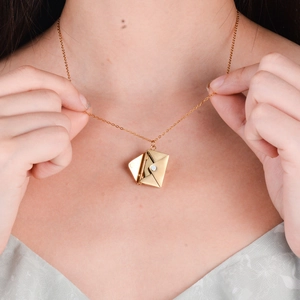 Elegant gold envelope pendant necklace with seal detail worn by a model on a slim chain