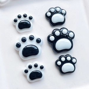 Detail view of black and white resin cat paw charms in three different sizes on white background