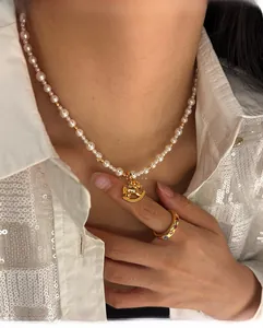 Close-up of pearl necklace with gold rocking horse pendant and colorful gem ring