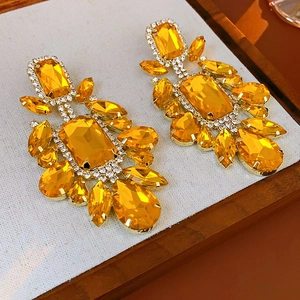 Macro detail of gold geometric drop earrings with amber crystals and sparkling rhinestones