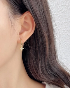 Close-up of gold clover earrings with inlaid crystals worn by a model in soft lighting