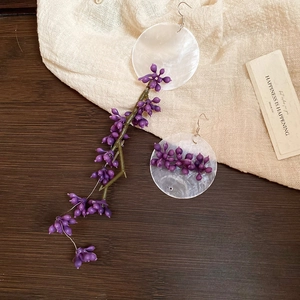 Detail of asymmetrical purple floral tassel earrings with shell inlay on wood and linen