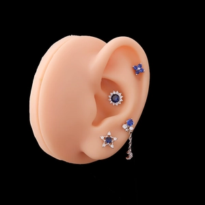 Detailed view of silver sunflower and star cartilage earrings with blue zircon on ear model