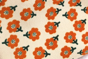 Close-up of floral corduroy fabric detail with orange flowers and green leaves pattern