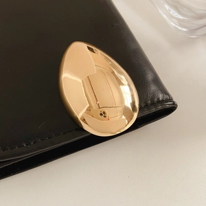 Nahaufnahme der goldenen Tropfenbrosche aus Metall auf schwarzem Leder mit glänzendem Finish