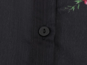Dettaglio camicia in chiffon nero con bottone rotondo e motivi floreali vivaci
